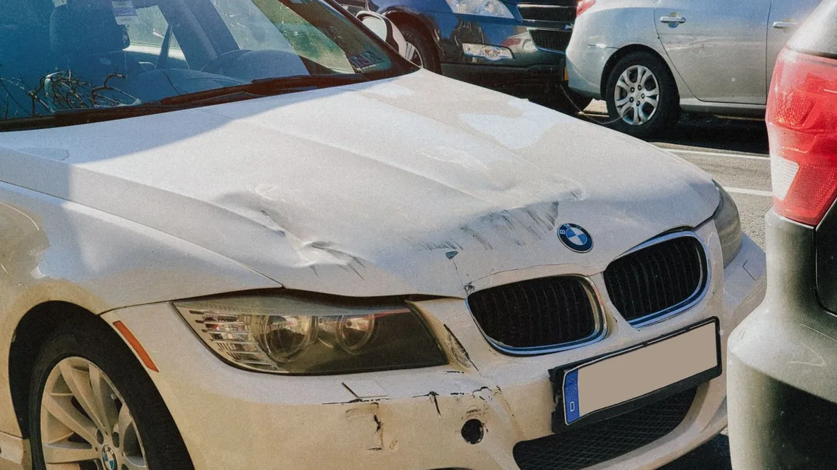 Auto blanco con el capó abollado y el parachoques rozado tras un choque leve en un estacionamiento